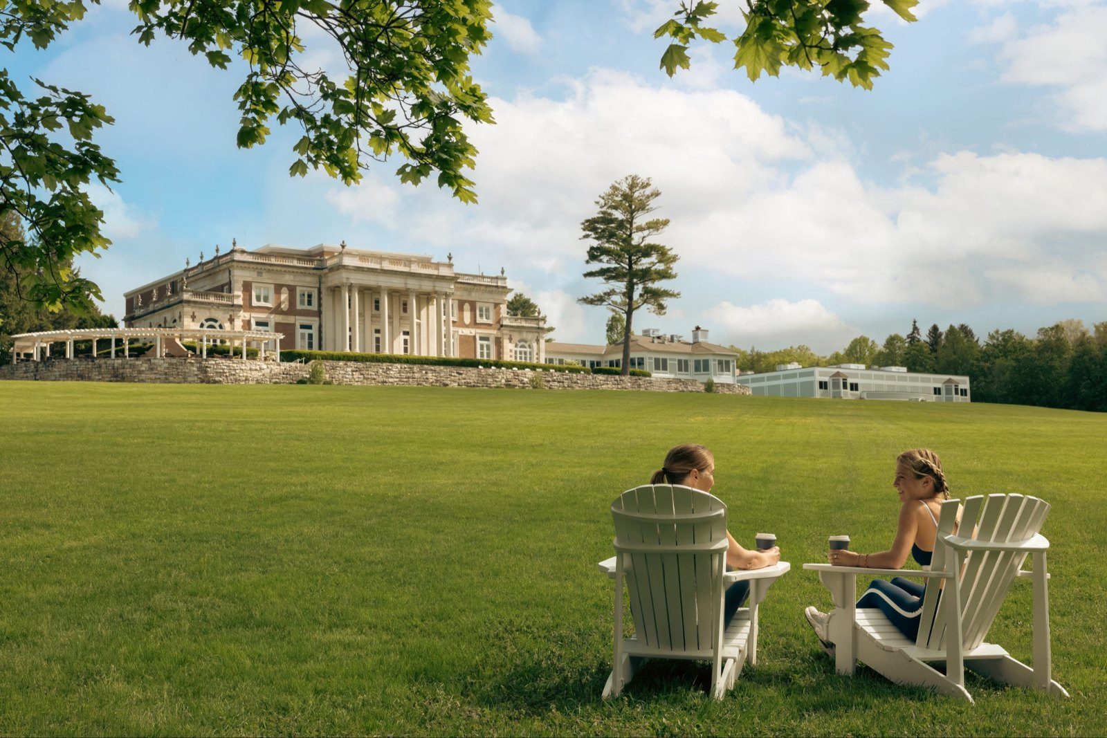Two women in Adirondack chairs on the lawn in front of the Canyon Ranch Lenox mansion
